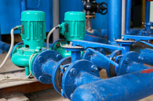 Diferentes tipos de bomba de água instalados em sistema hidráulico industrial com tubulações e válvulas de controle.